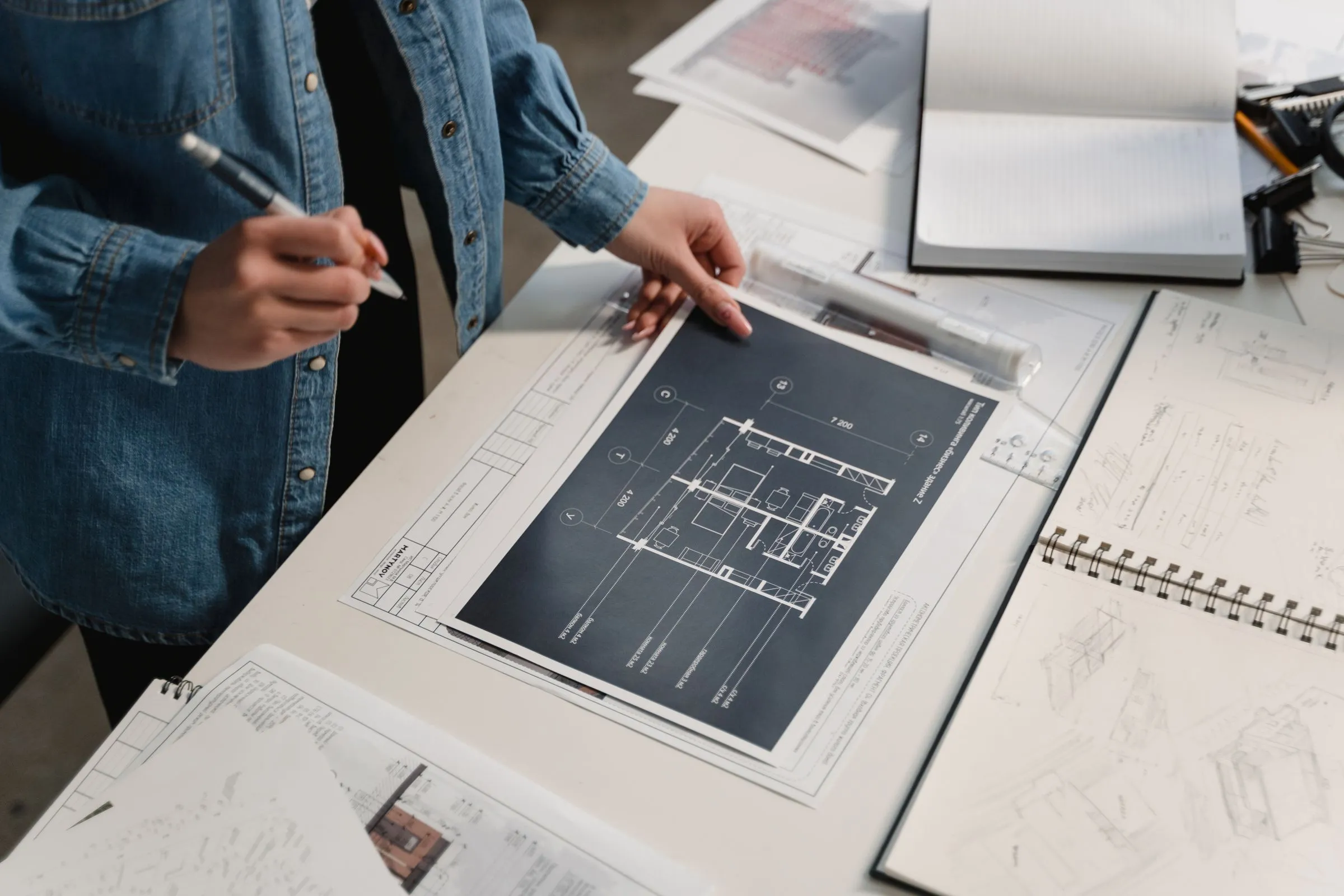 A person reviewing a blueprint and planning documents spread across a desk